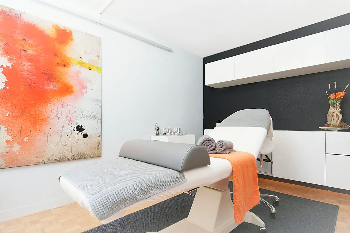 Behandlungsraum von Facezination mit Liege und orangem Wandbild